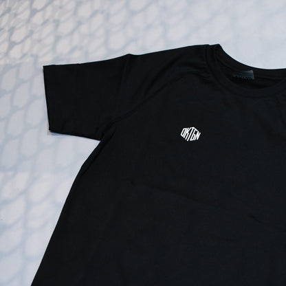 Shooting réel OKTGN — rashguard classique noir posé, détail du tissu et du logo, sans drapeau