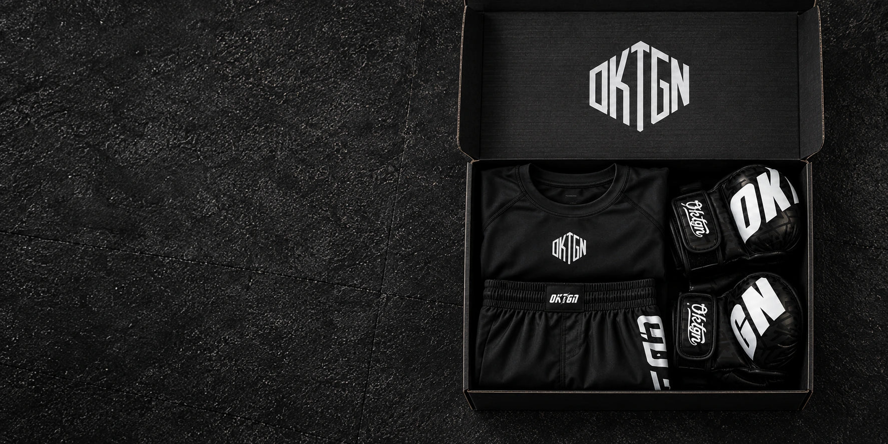 Mise en scène du pack : carton au logo OKTAGON, rashguard, short et gants MMA noirs